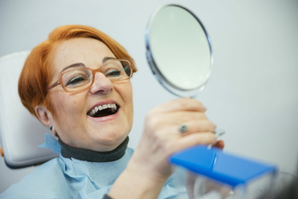 older woman looking in the mirror at her new dentures